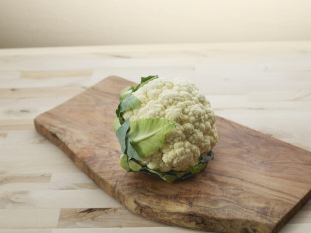 Whole fresh cauliflower on a curved wooden board, close-up