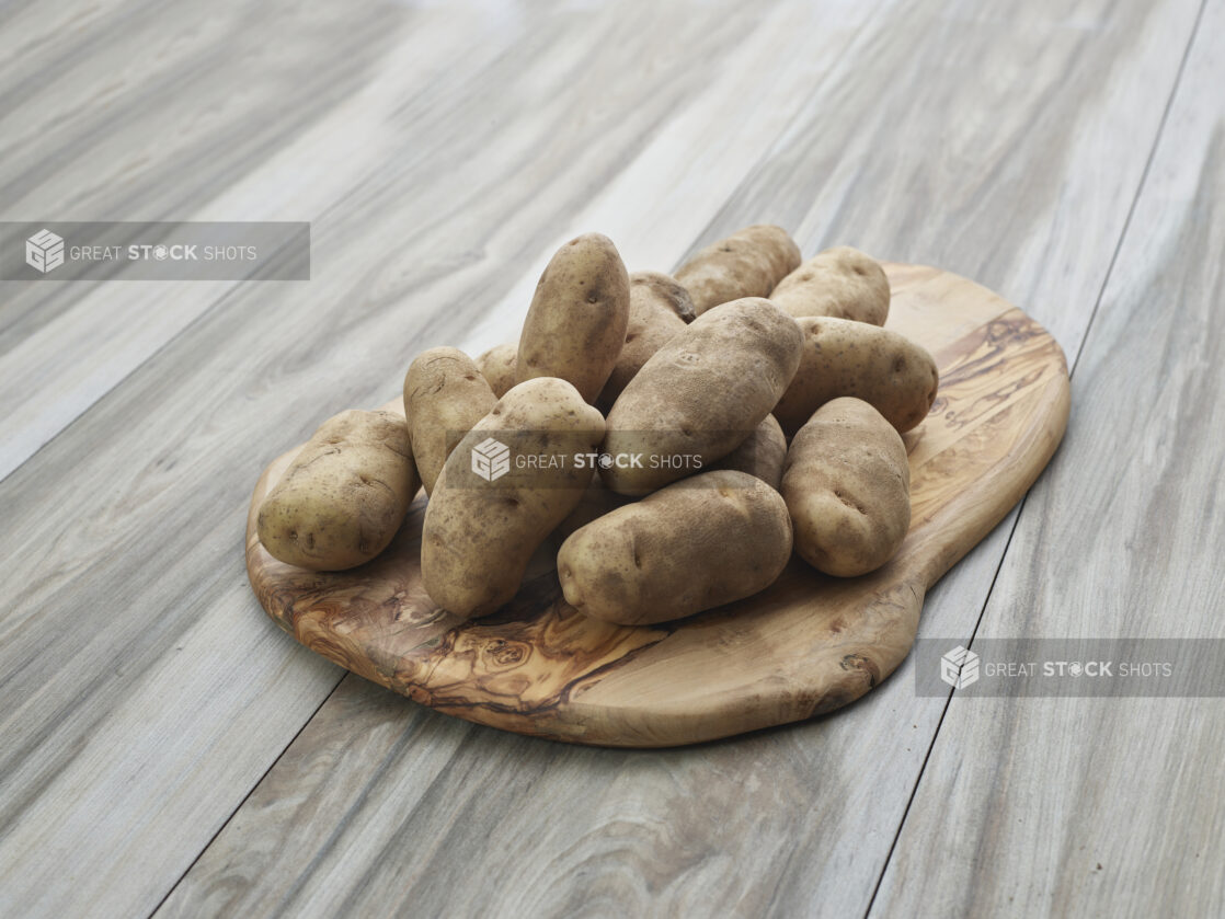 Whole russet potatoes piled on a rounded wooden board, close-up