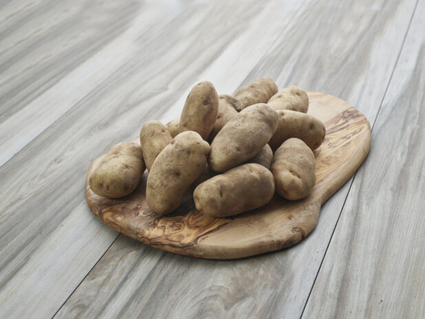 Whole russet potatoes piled on a rounded wooden board, close-up