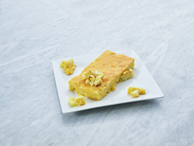 Rectangular slice of baked cauliflower macaroni and cheese on a square white plate, marble background