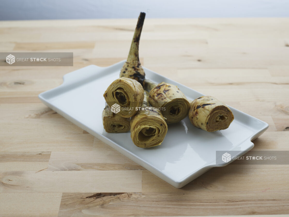 Grilled artichoke hearts on a rectangular white ceramic platter, close-up