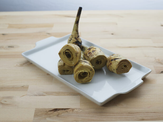 Grilled artichoke hearts on a rectangular white ceramic platter, close-up