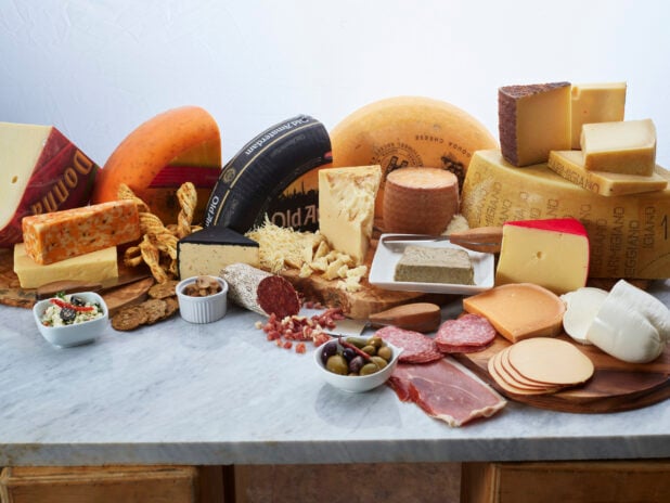 Spread of various cheeses and cured meats on a white marble counter