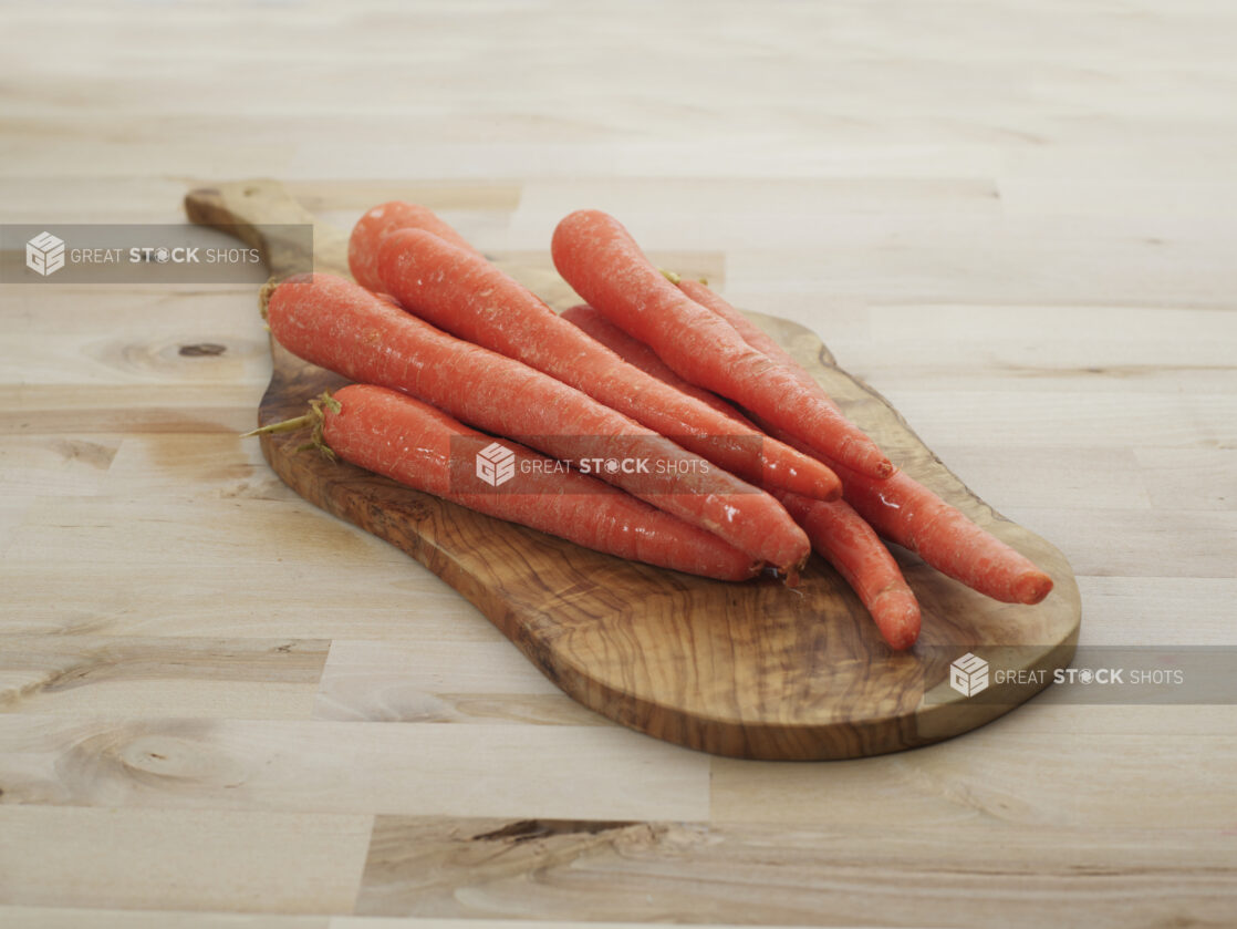 Orange carrots piled on a rounded wooden paddle, close-up