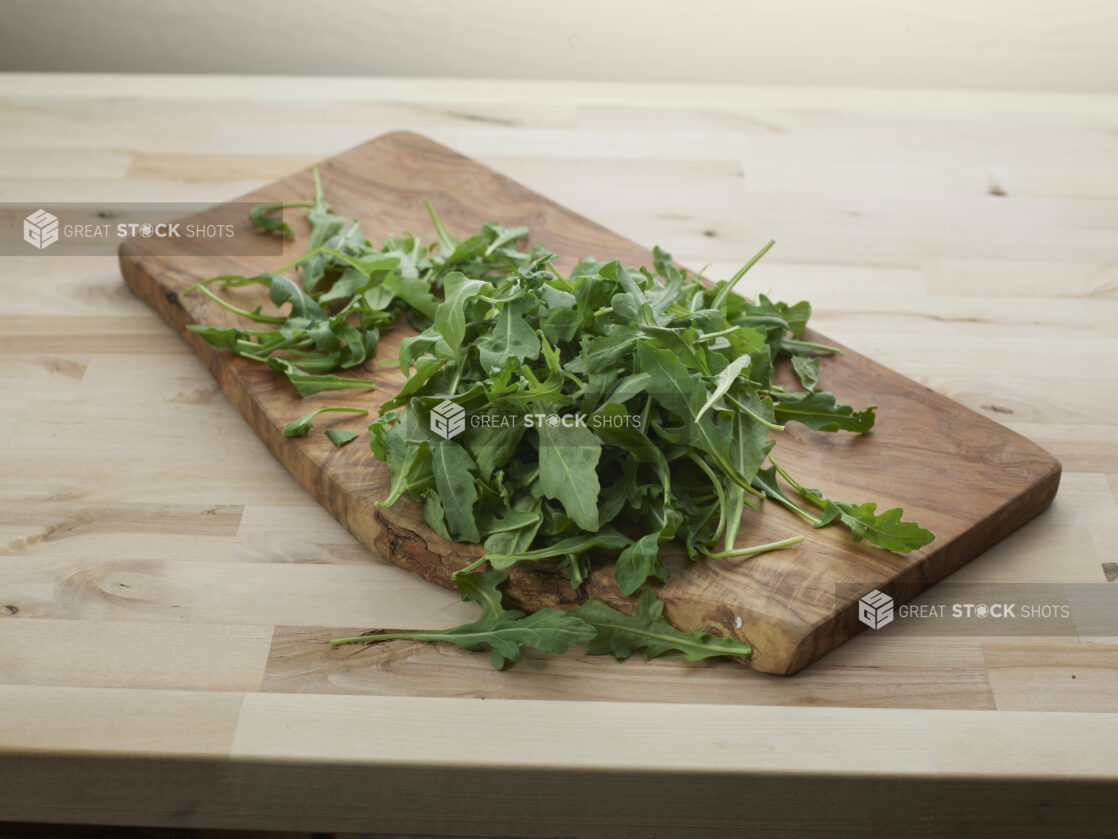 Fresh arugula piled on a wood paddle