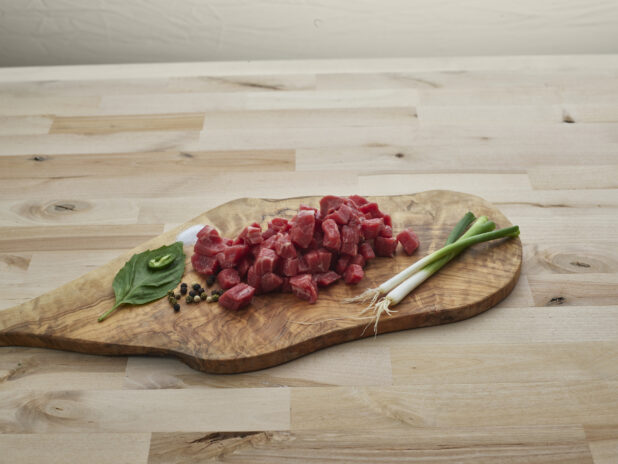 Diced fresh red meat with seasonings on a natural wood board, close-up