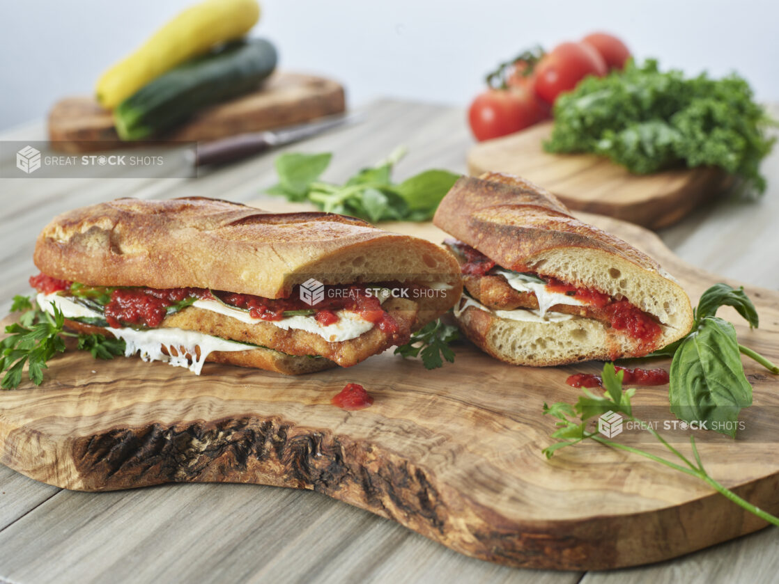 Veal or Chicken Cutlet Parmesan Sandwiches with Melted Mozzarella, Fresh Basil and Marinara Sauce on Ciabatta Bread on a Wooden Cutting Board