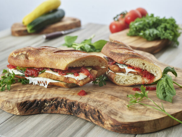Veal or Chicken Cutlet Parmesan Sandwiches with Melted Mozzarella, Fresh Basil and Marinara Sauce on Ciabatta Bread on a Wooden Cutting Board