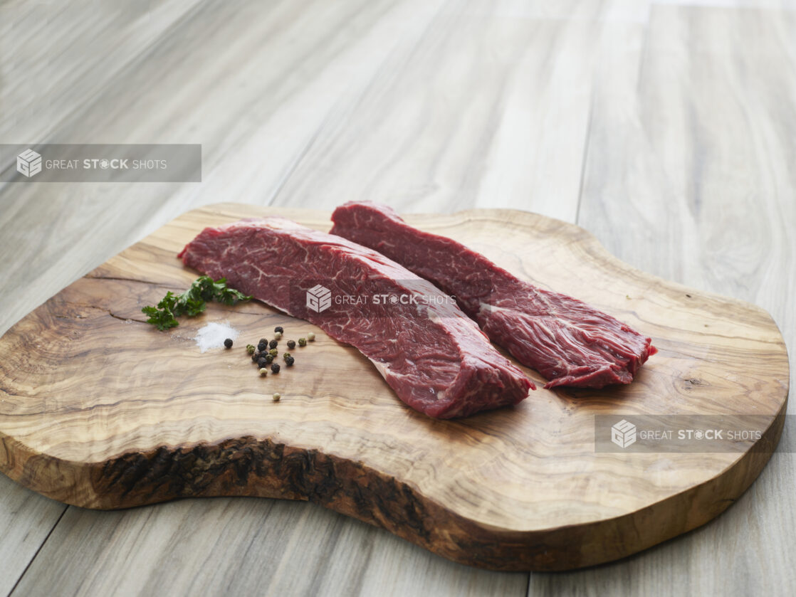 Two raw hanger steaks with seasonings on a natural wood board, close-up, variation 2