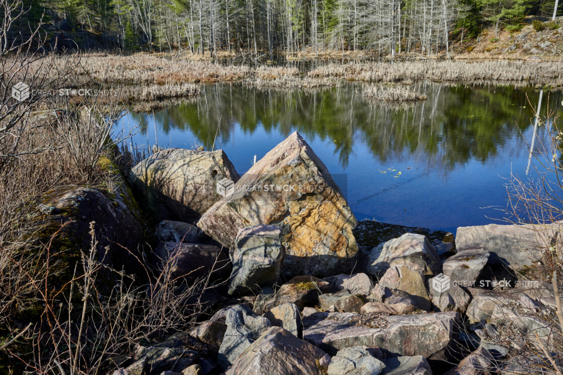 View of Rocks and Boulders by a Lake Lined with Pine Trees and Evergreens in Cottage Country, Ontario, Canada