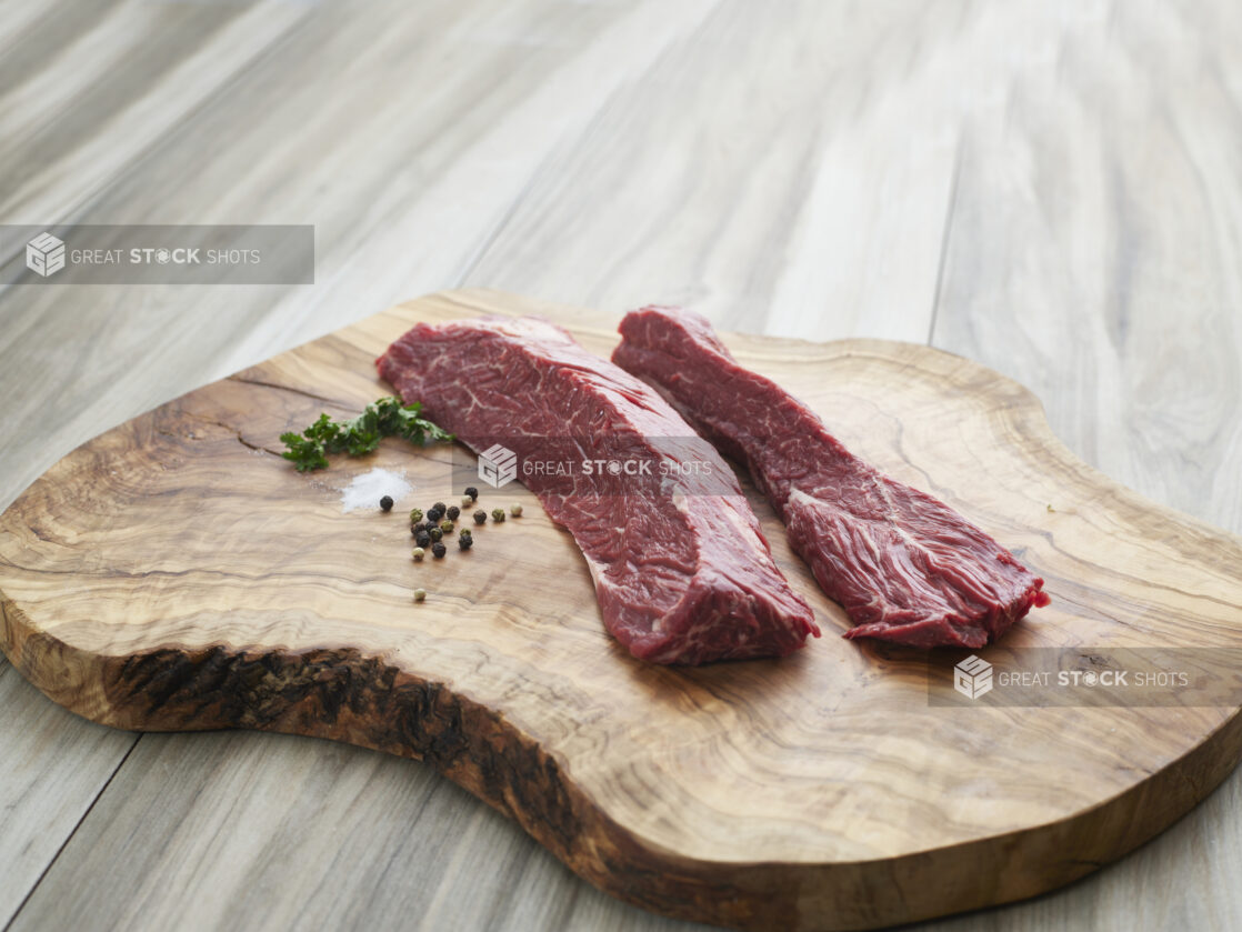 Two raw hanger steaks with seasonings on a natural wood board, close-up, variation 1