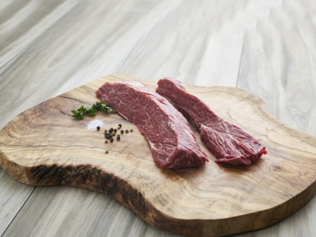 Two raw hanger steaks with seasonings on a natural wood board, close-up, variation 1