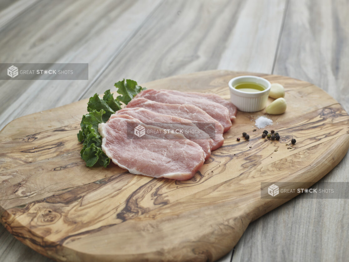 Raw boneless pork arranged on a wood board with seasonings