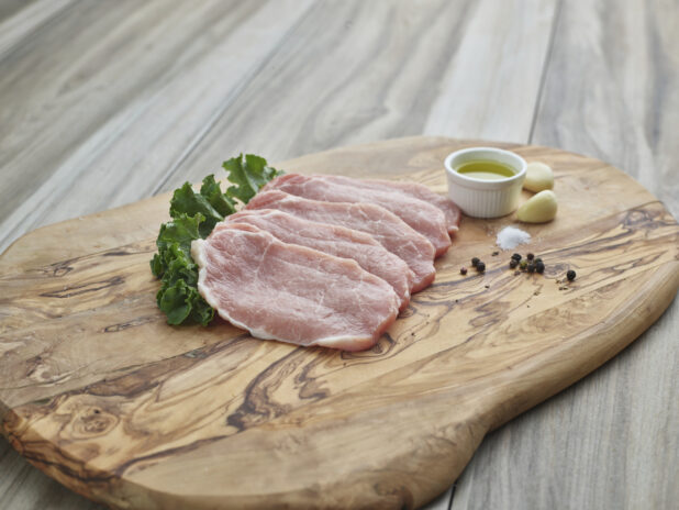 Raw boneless pork arranged on a wood board with seasonings