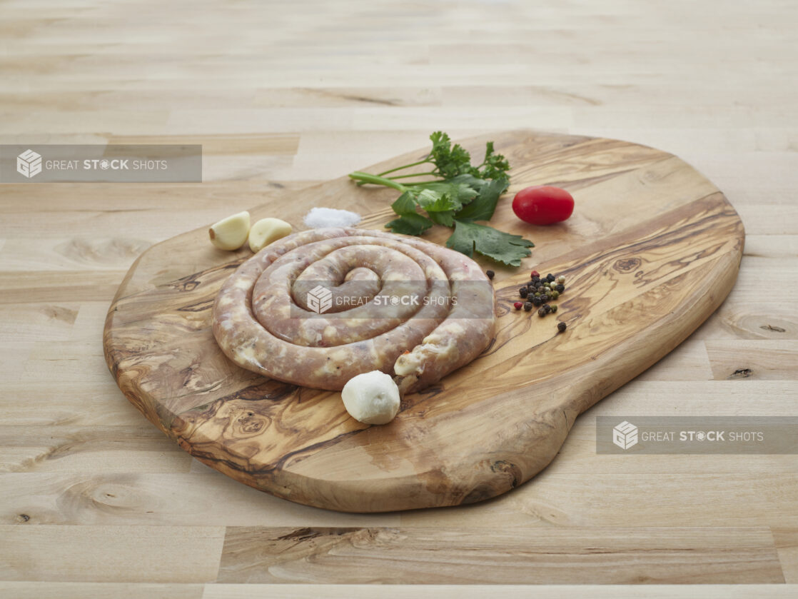 Pork sausage coil on a wood board with seasonings surrounding, close-up