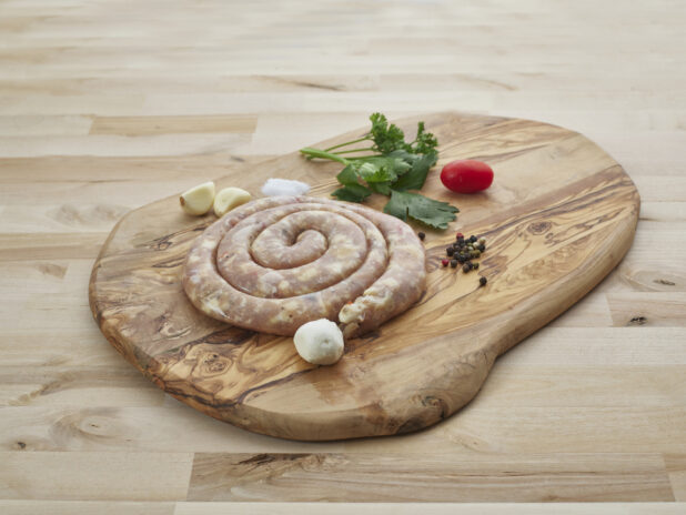 Pork sausage coil on a wood board with seasonings surrounding, close-up