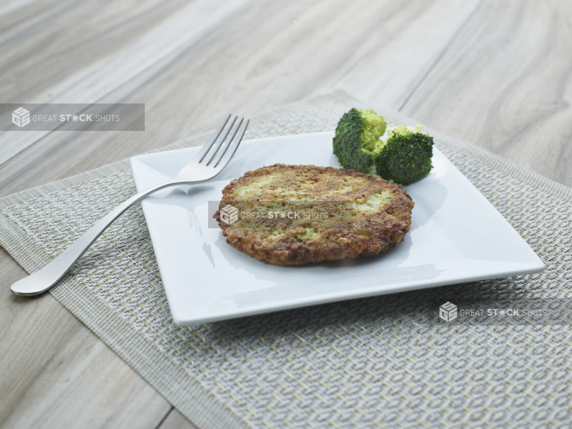 Golden fried broccoli cake with florets on a square white plate, close-up