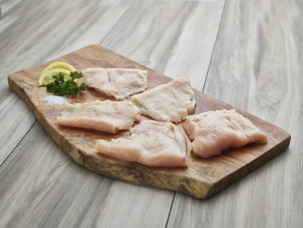 Five thinly sliced chicken cutlets with seasonings on a natural wood board, close-up