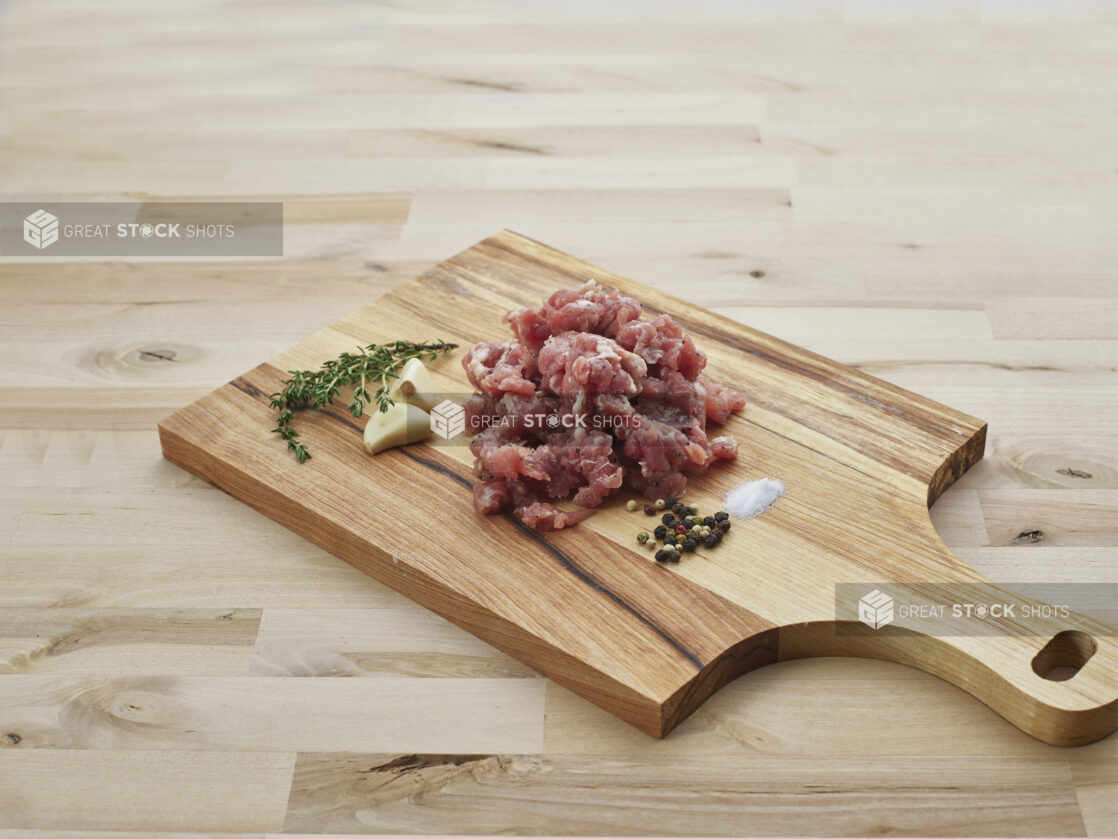 Ground sausage meat piled on a wood paddle with seasonings, close-up