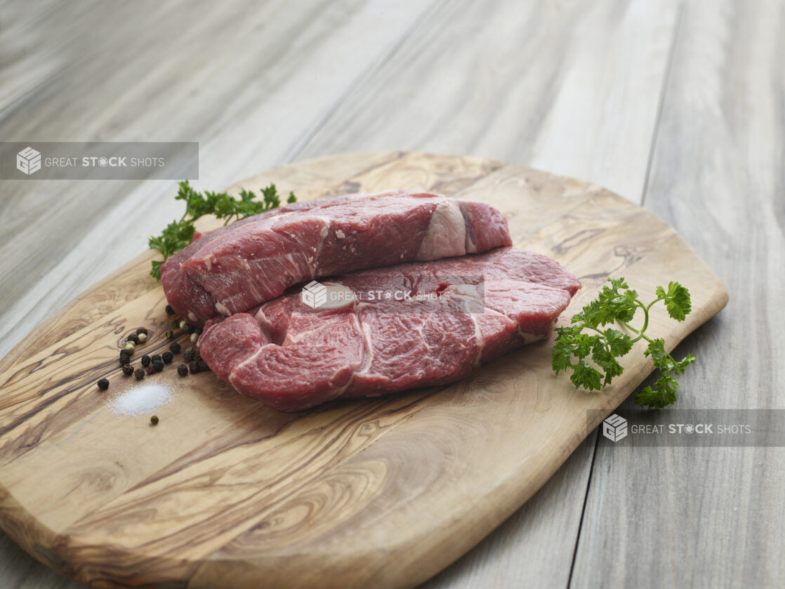 Two steaks cut from leg of lamb on a natural wood board with seasonings