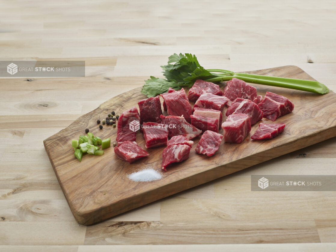 Chunks of stewing chuck on a wood cutting board with seasonings