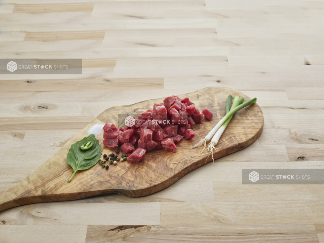 Diced fresh red meat with seasonings on a natural wood board, close-up