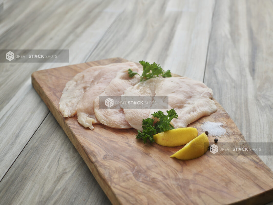 Thinly sliced raw chicken cutlets with seasonings on a natural wood board, close-up