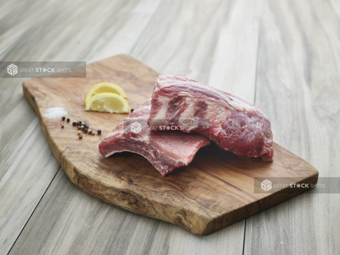 Small rack of baby back ribs, halved on natural wood cutting board with seasonings, close-up