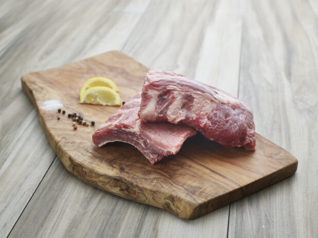 Small rack of baby back ribs, halved on natural wood cutting board with seasonings, close-up