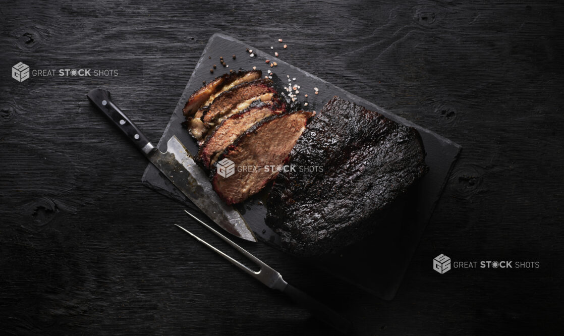 Smoked brisket with knife, partially sliced, overhead view