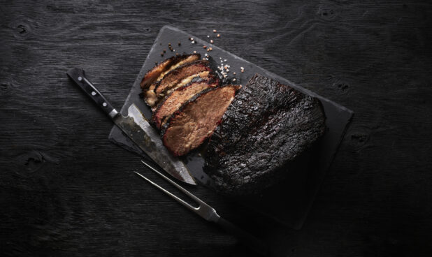 Smoked brisket with knife, partially sliced, overhead view