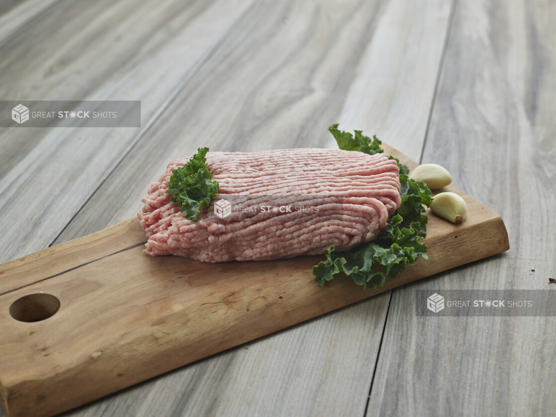 Raw ground pork with cloves of garlic on a wooden board, close-up, variation 2