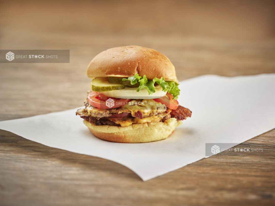 Double smash burger with bacon, cheddar and the works on white parchment paper, wood background