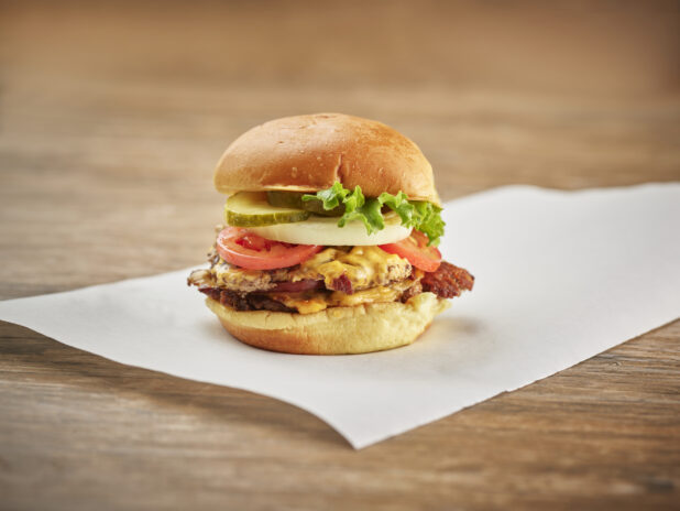 Double smash burger with bacon, cheddar and the works on white parchment paper, wood background