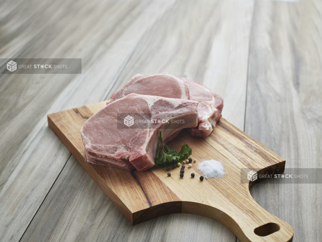 Two thick center cut pork chops with seasonings on a wooden paddle