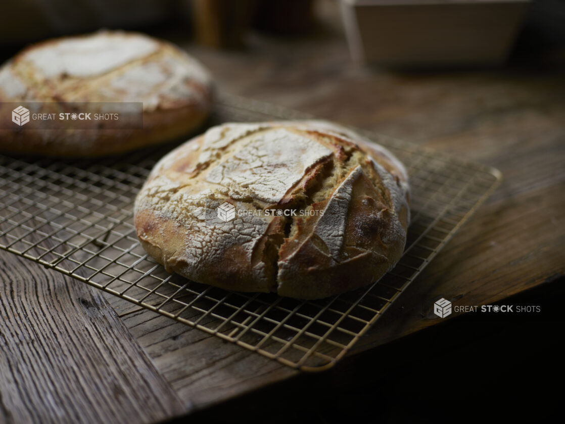 Round Loaves of Sourdough Bread Cooling on a Wire Rack on a Rustic Wooden Table in an Indoor Setting