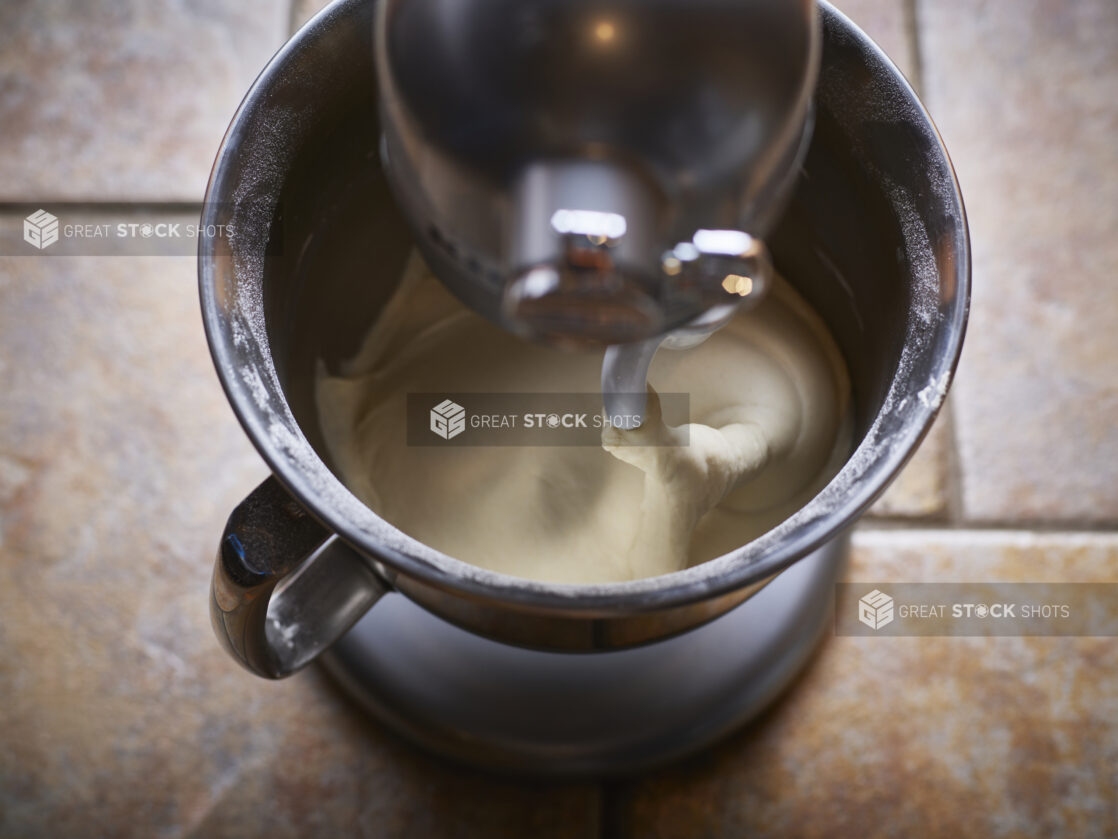 Stainless steel stand mixer with dough hook partially submersed in soft dough, overhead