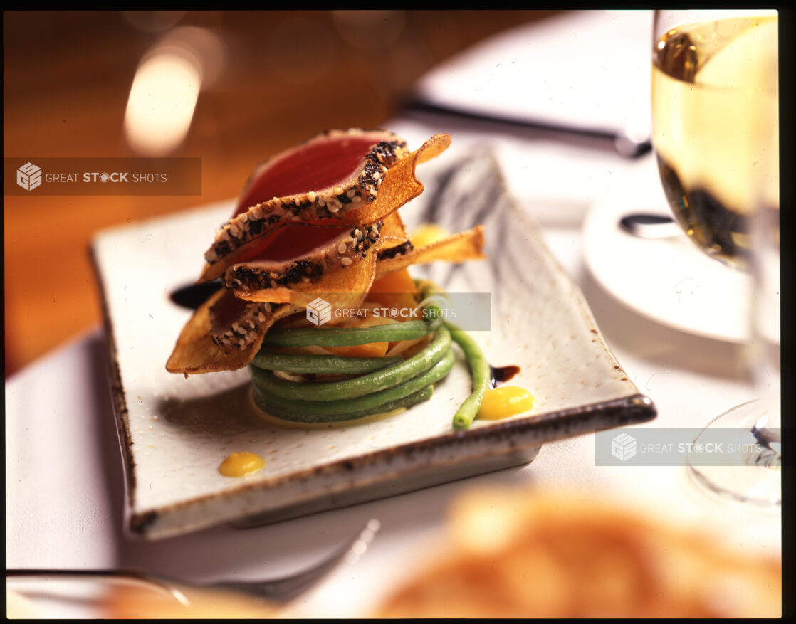 Sesame Crusted Seared Tuna Tataki With Sweet Potato Chips and Green String Beans on a Ceramic Dish in a Restaurant Setting