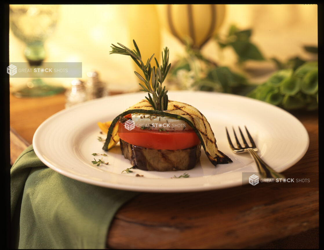 Vegetable Napoleon with Grilled Zucchini and Eggplants, Tomato and Goat Cheese on a White Ceramic Plate in an Indoor Setting