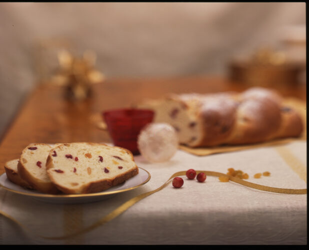 Sliced Dried Fruit Bread on a Gold-Trimmed Plate with Christmas Holiday Decorations on a Wooden Kitchen Table