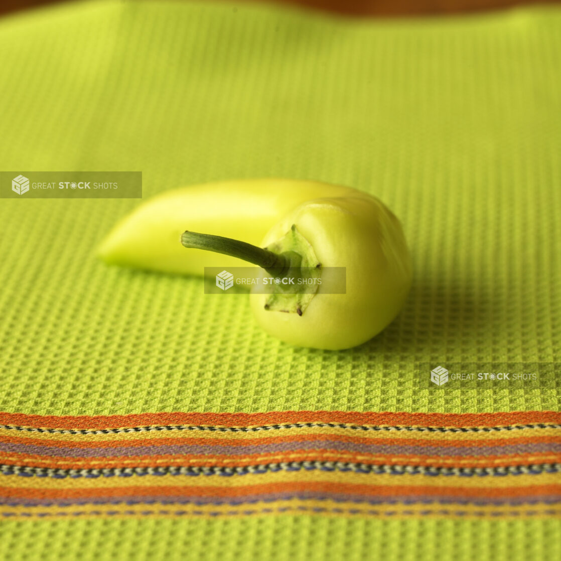 Close Up of a Green Banana Pepper on a Lime Green Tea Towel in an Indoor Setting