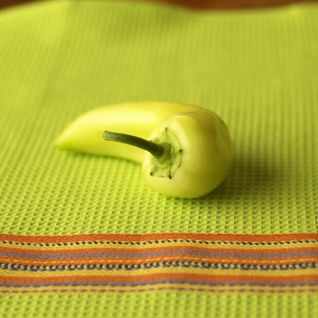 Close Up of a Green Banana Pepper on a Lime Green Tea Towel in an Indoor Setting