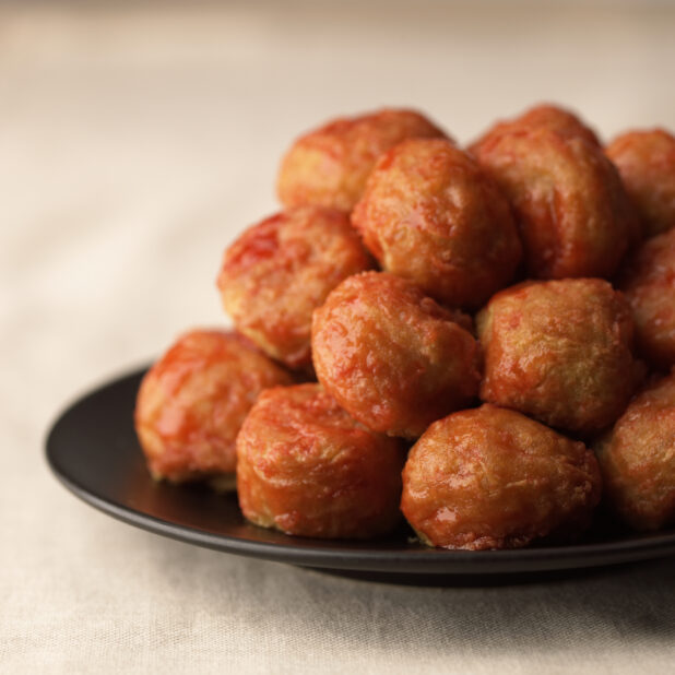 Close Up of a Dish of Chinese Sweet and Sour Meatballs Stacked on a Black Ceramic Plate