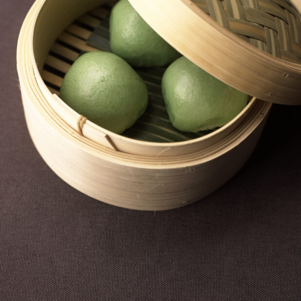 Close Up of a Dum Sum Bamboo Steamer with Fluffy Green Steamed Buns or Bao