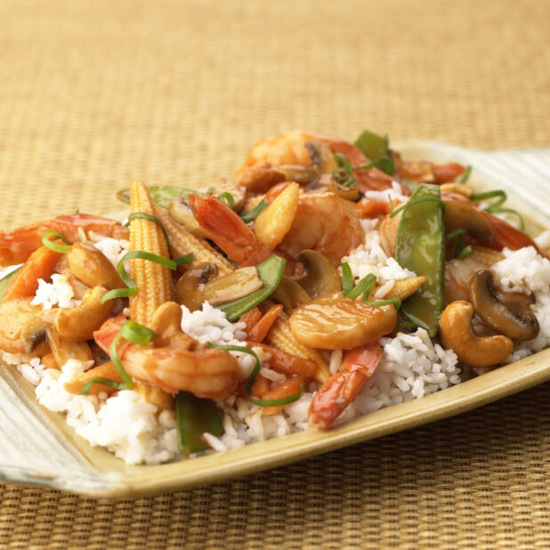 Close Up of a Dish of Shrimp, Vegetable and Cashew Stir Fry Over Rice in a Yellow Ceramic Platter