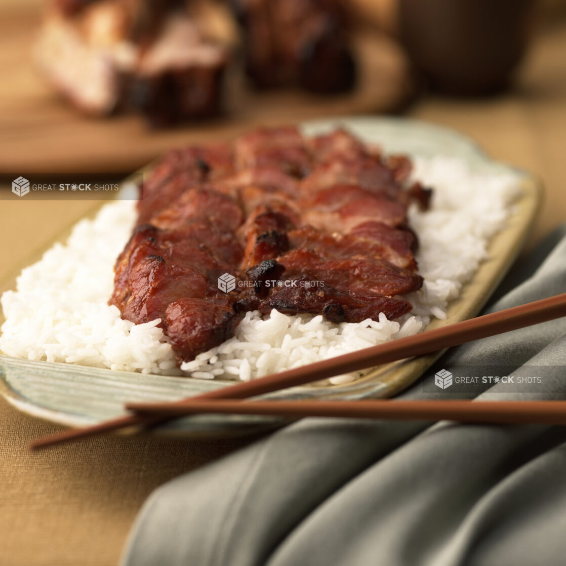 Close Up of a Dish of Honey-Glazed BBQ Pork Over White Rice on a Yellow Ceramic Platter