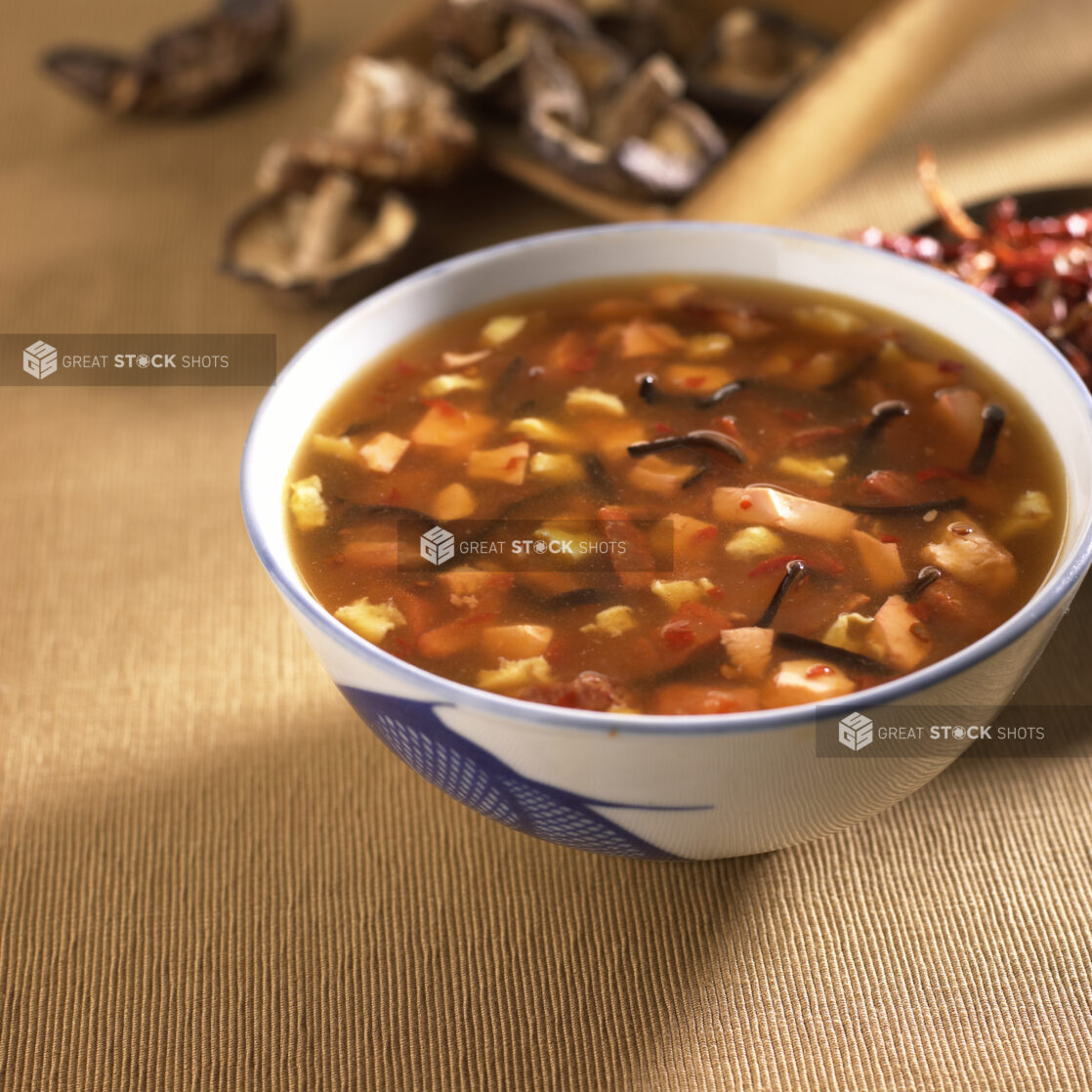 Close Up of a Ceramic Bowl of Chinese Hot and Sour Soup with Black Fungus Mushrooms and Chopped Tofu