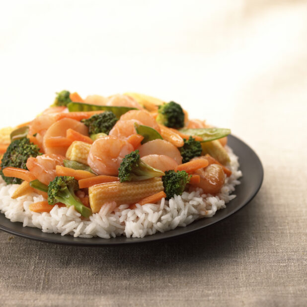 Close Up of a Dish of Shrimp and Vegetable Stir Fry Over White Rice on a Black Ceramic Plate