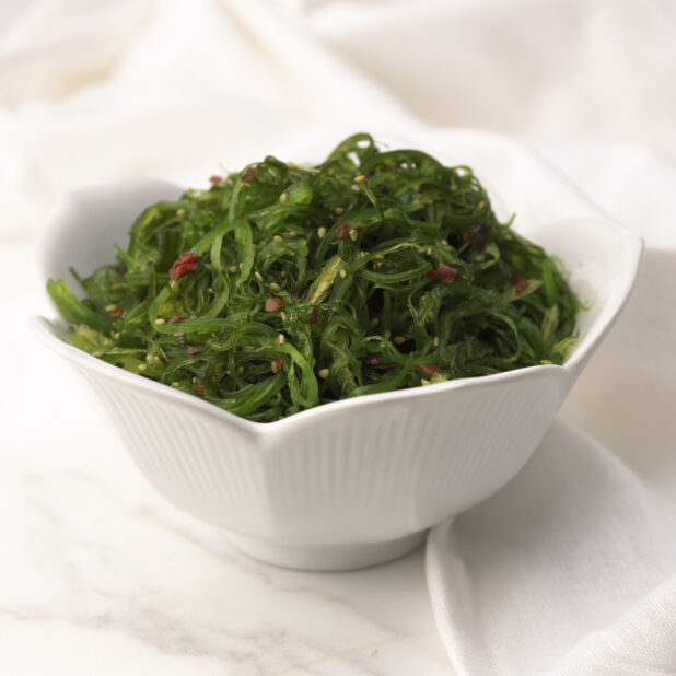 Close Up of a White Ceramic Bowl of Seaweed Salad on a Marble Surface