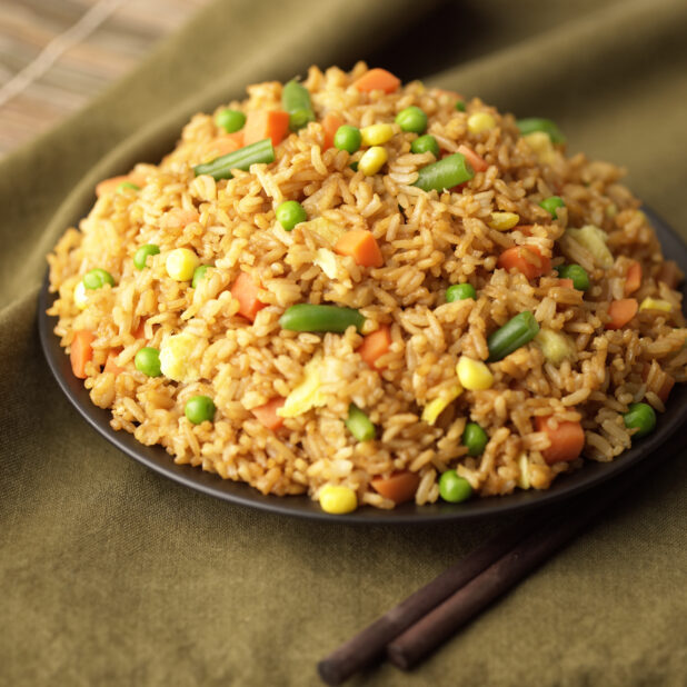 Close Up of a Dish of Chinese Fried Rice with Green Beans, Corn and Carrots on a Black Ceramic Plate